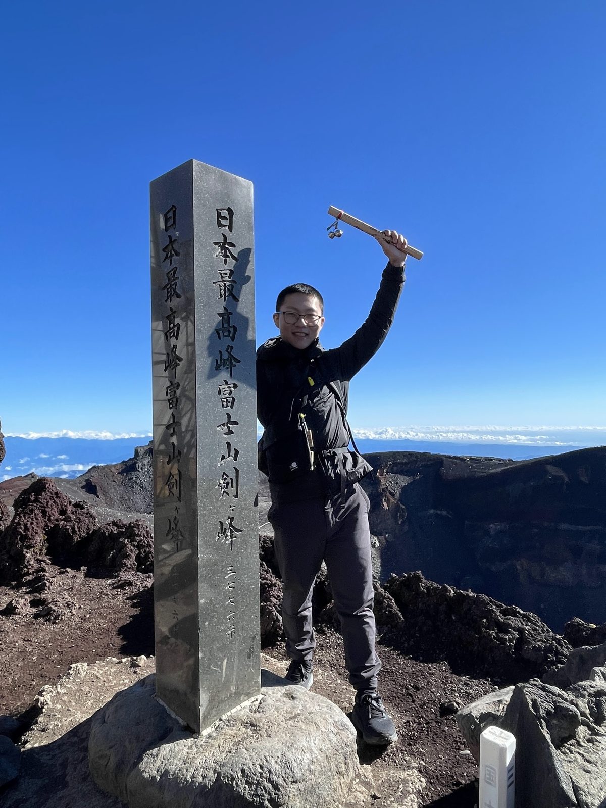 站在富士山頂石碑旁舉起金剛杖的人